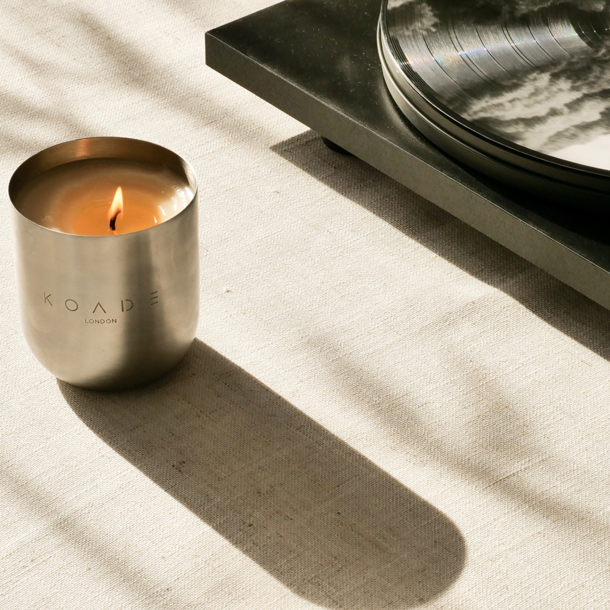 Candle in a metallic container with 'Koade London' branding on a textured surface.