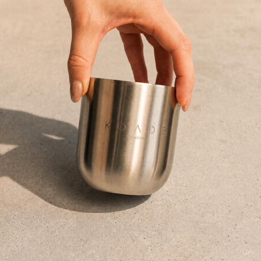 Hand holding a stainless steel cup with 'Koade London' branding on a neutral background