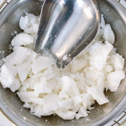 Chunks of natural candle wax in a glass bowl with a metal scoop