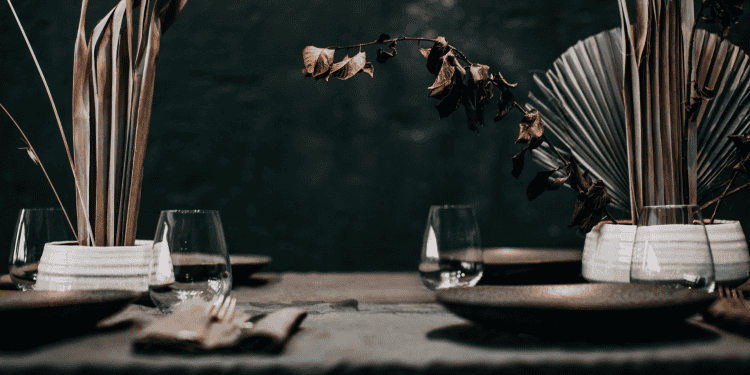 Dining table setting with glasses, plates, and decorative plants against a dark background