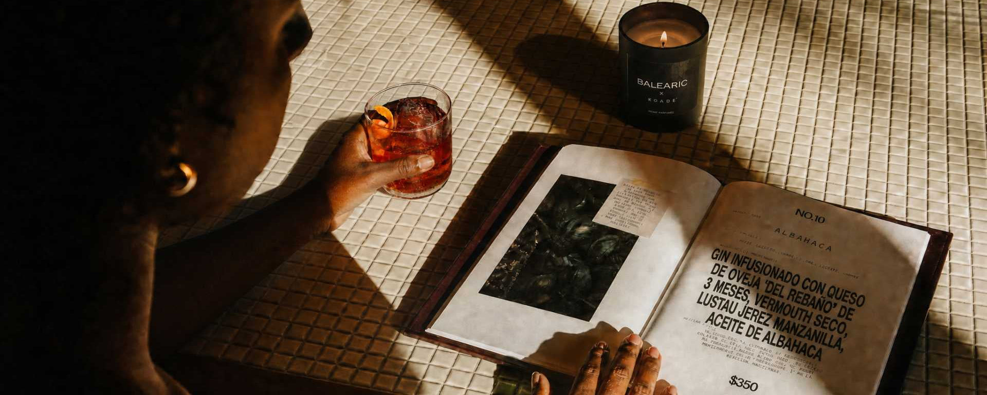 Person reading a book with a candle and glass of wine on a tiled surface