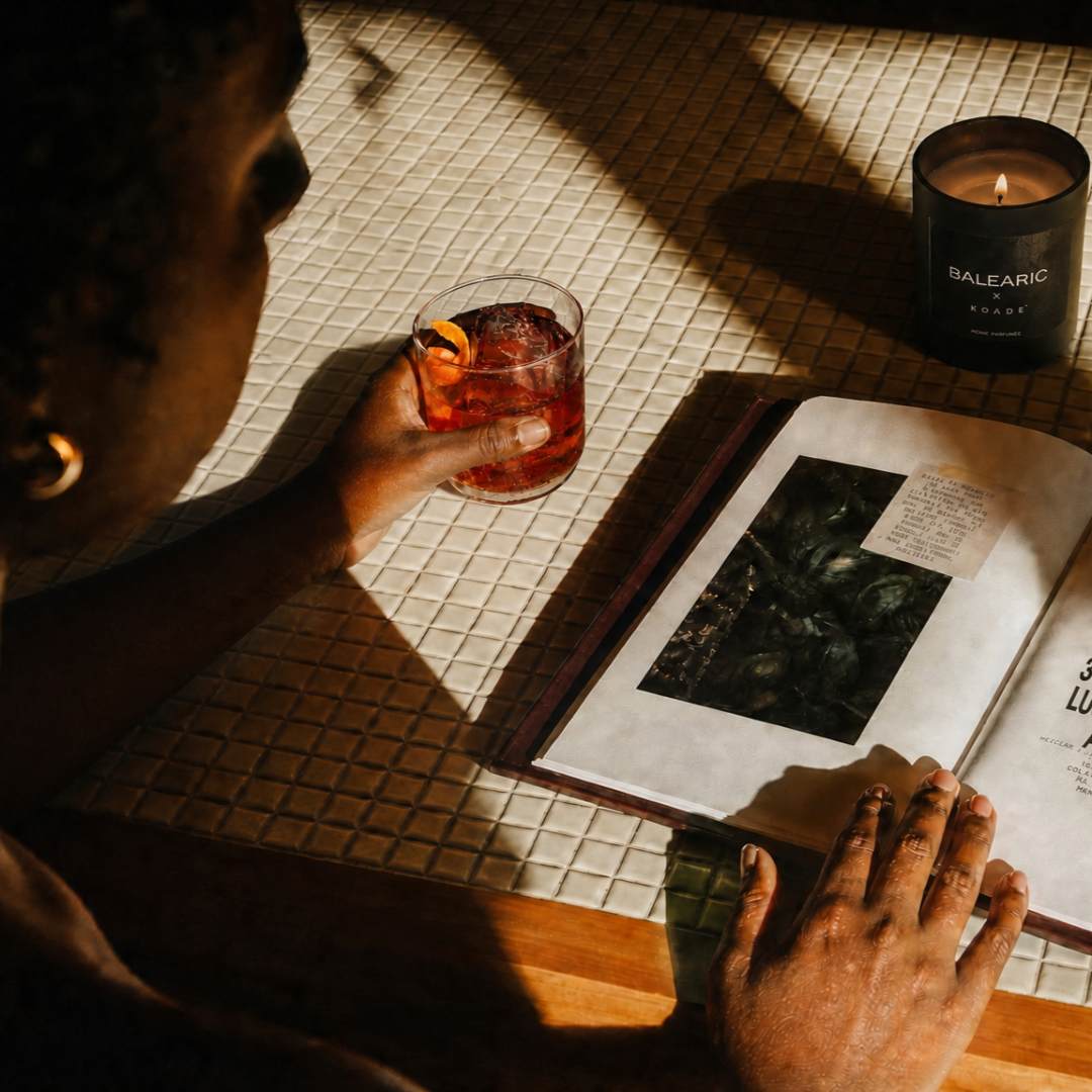 Person holding a cocktail glass with a candle and open book on a table