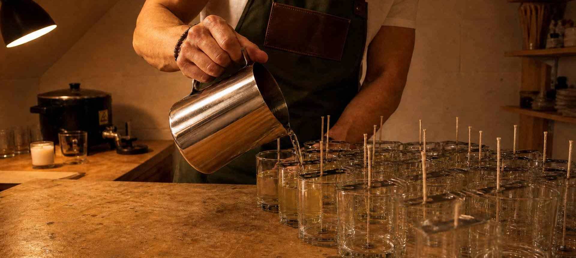 Person pouring liquid into glasses on a wooden counter.