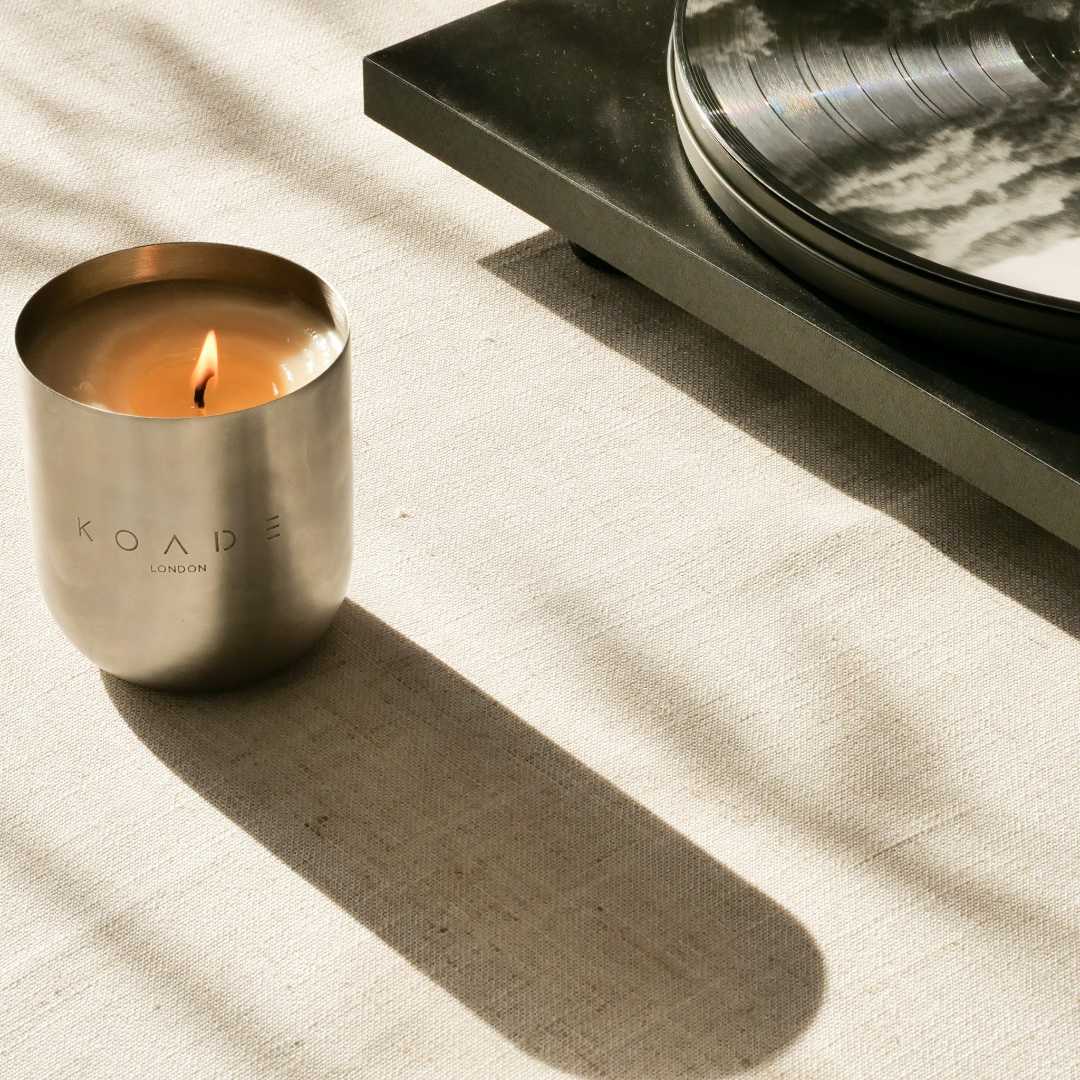 Candle in a metallic container with 'KOADE London' branding on a textured surface.