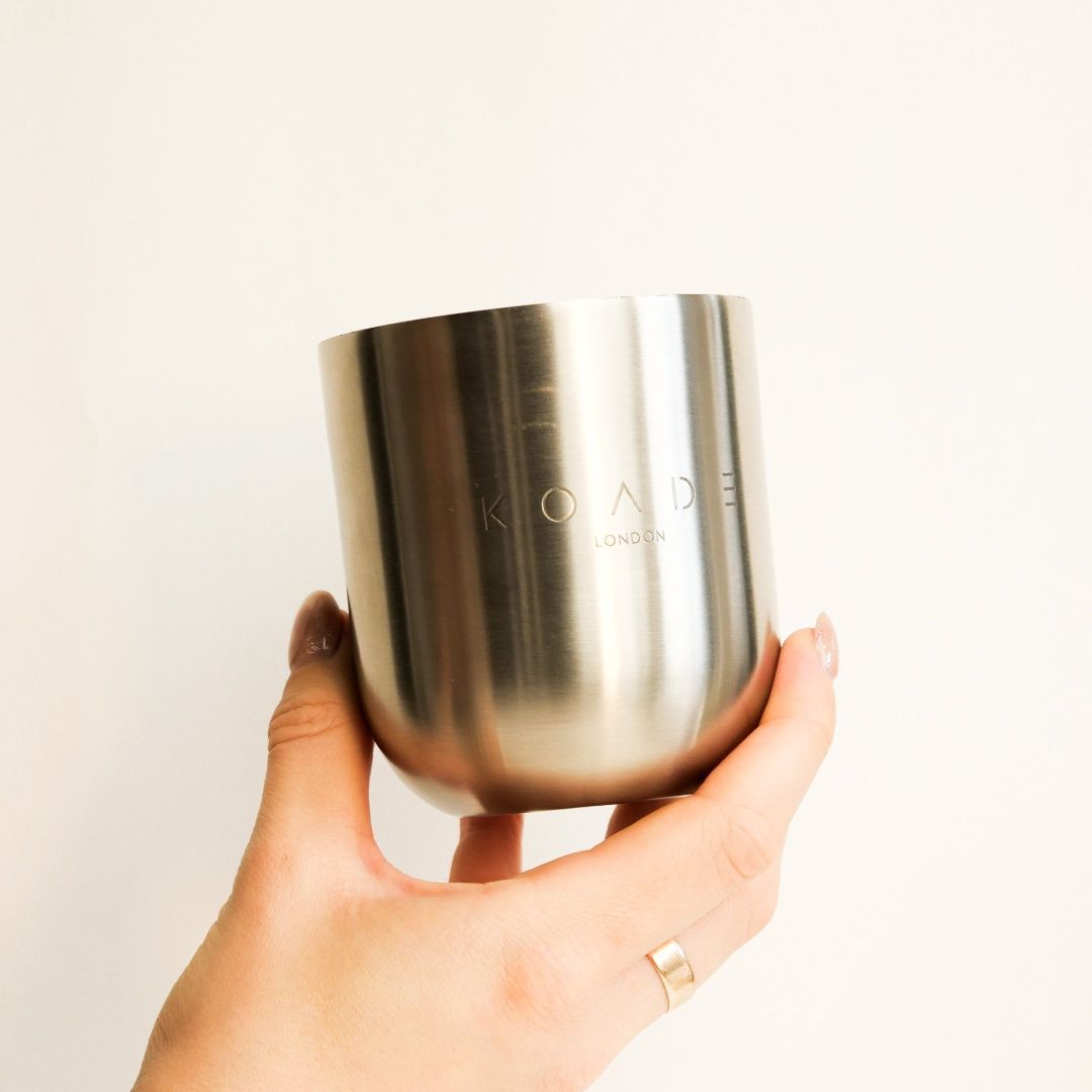 Hand holding a silver tumbler with 'KOADE' branding against a light background