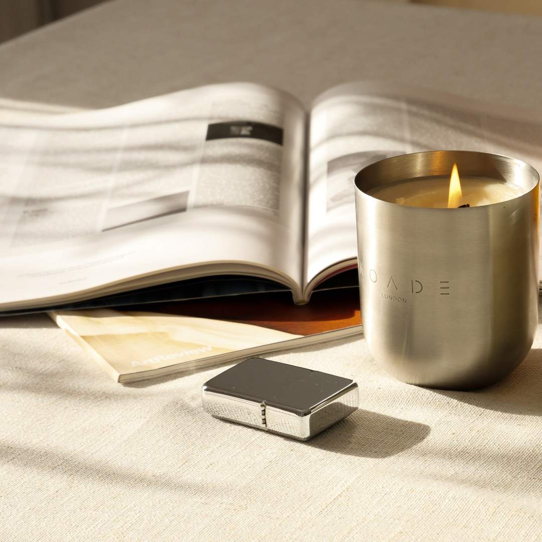 Silver candle holder with a lit candle on a table next to an open book