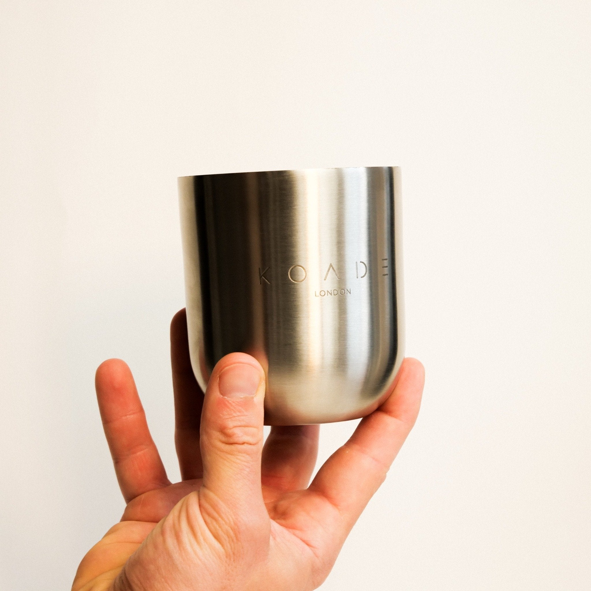 Hand holding a silver cylindrical container with 'KOADE' branding on a light background