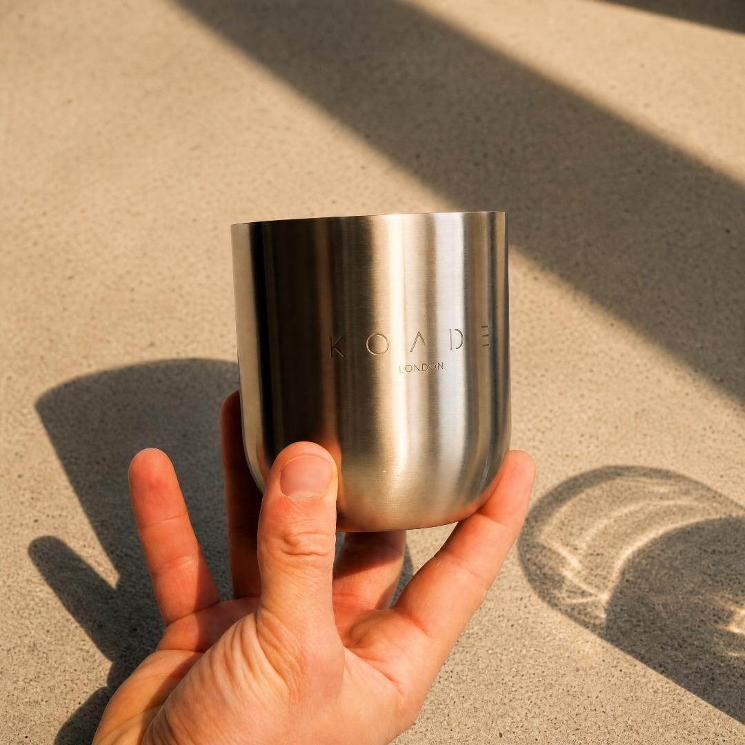 Hand holding a silver tumbler with 'Koade' branding on a sandy background