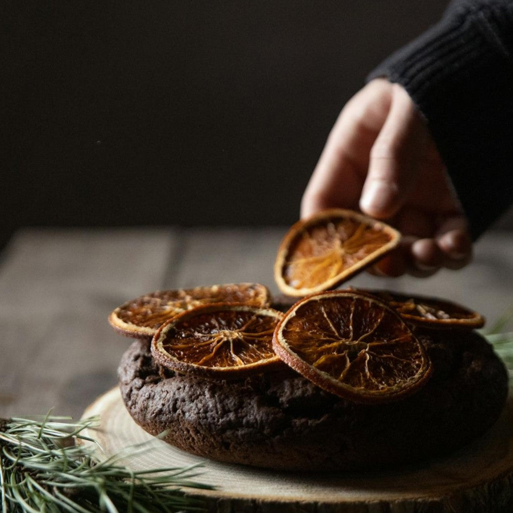 Hand picking dried orange slices from a chocolate dessert on a wooden board.