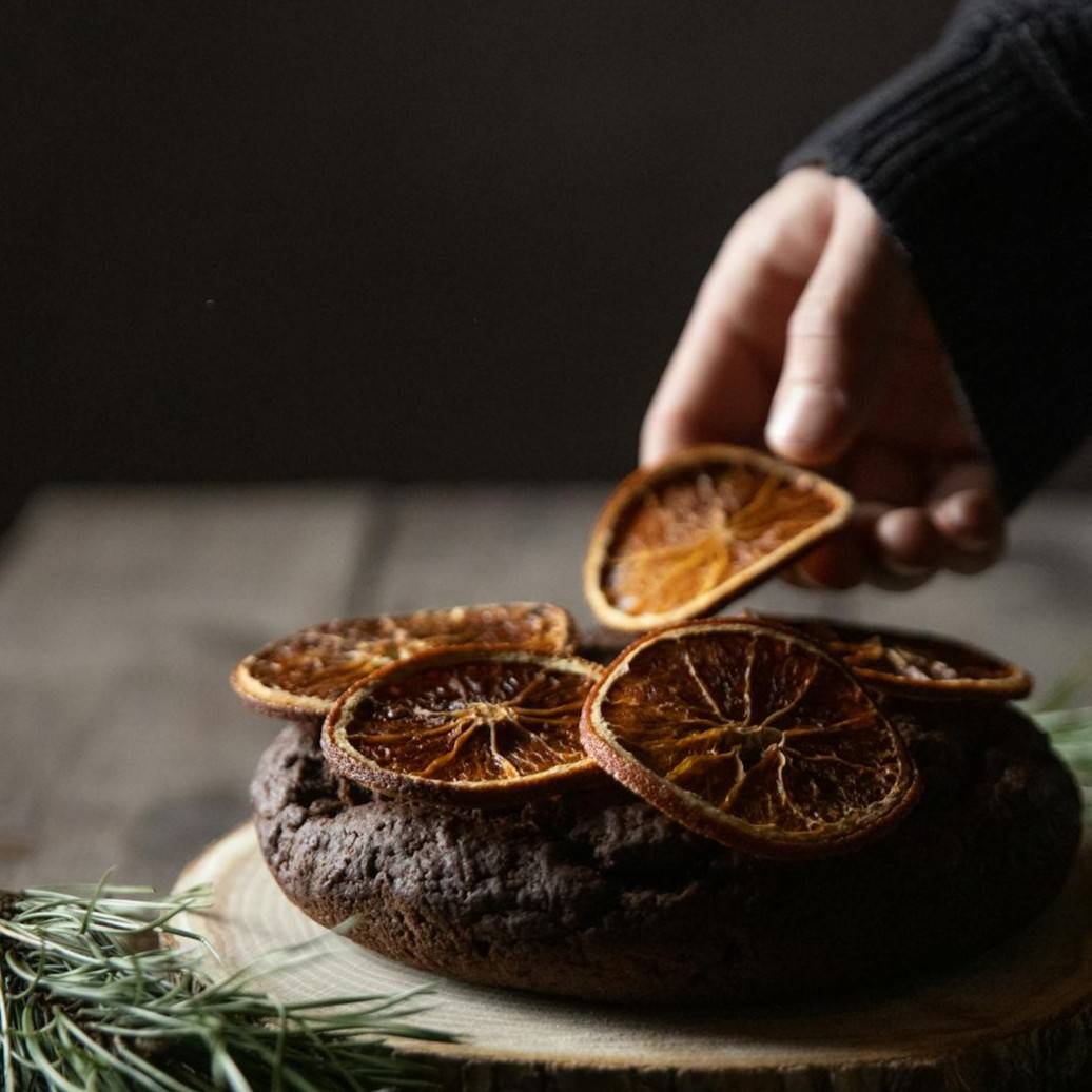 Hand picking dried orange slices from a chocolate dessert on a wooden board.