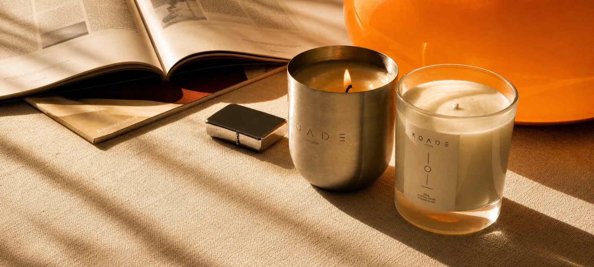 Two candles on a table with an open book and smartphone in the background.
