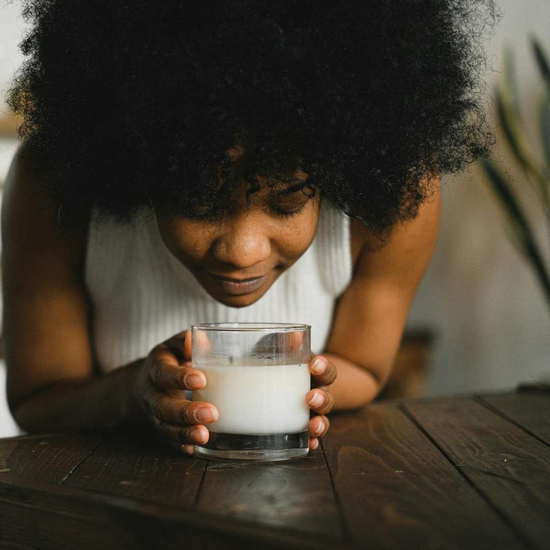Person holding a glass of milk on a wooden table