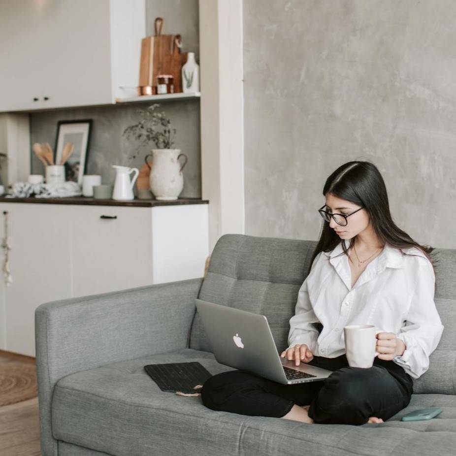 Lady wearing a white top sat on a grey couch