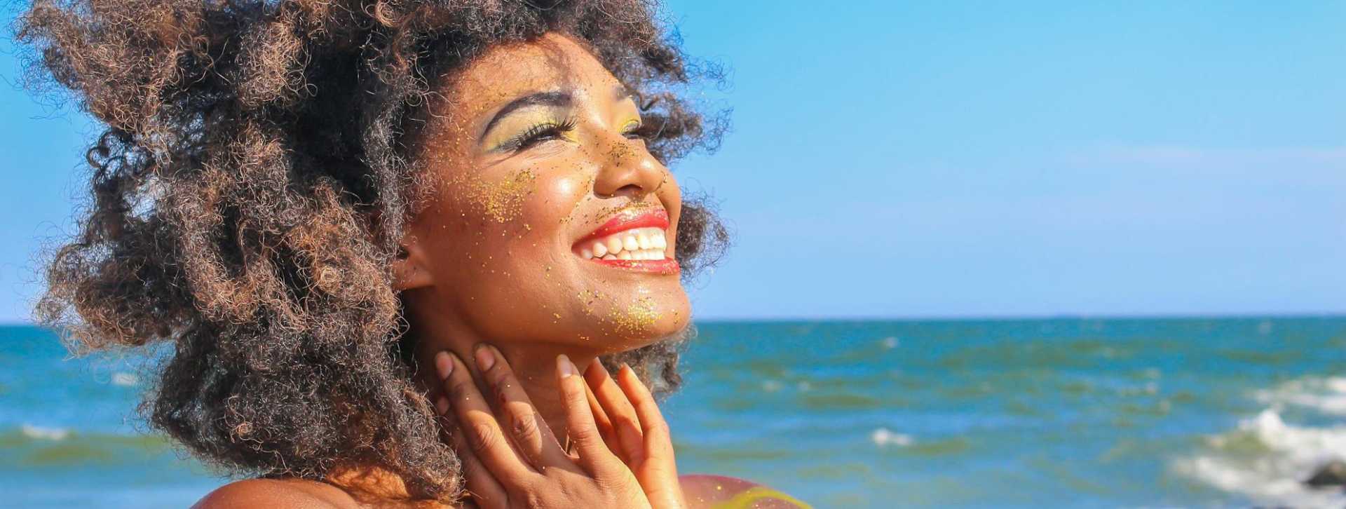 Lady smiling in the sunshine on a beach next to the sea