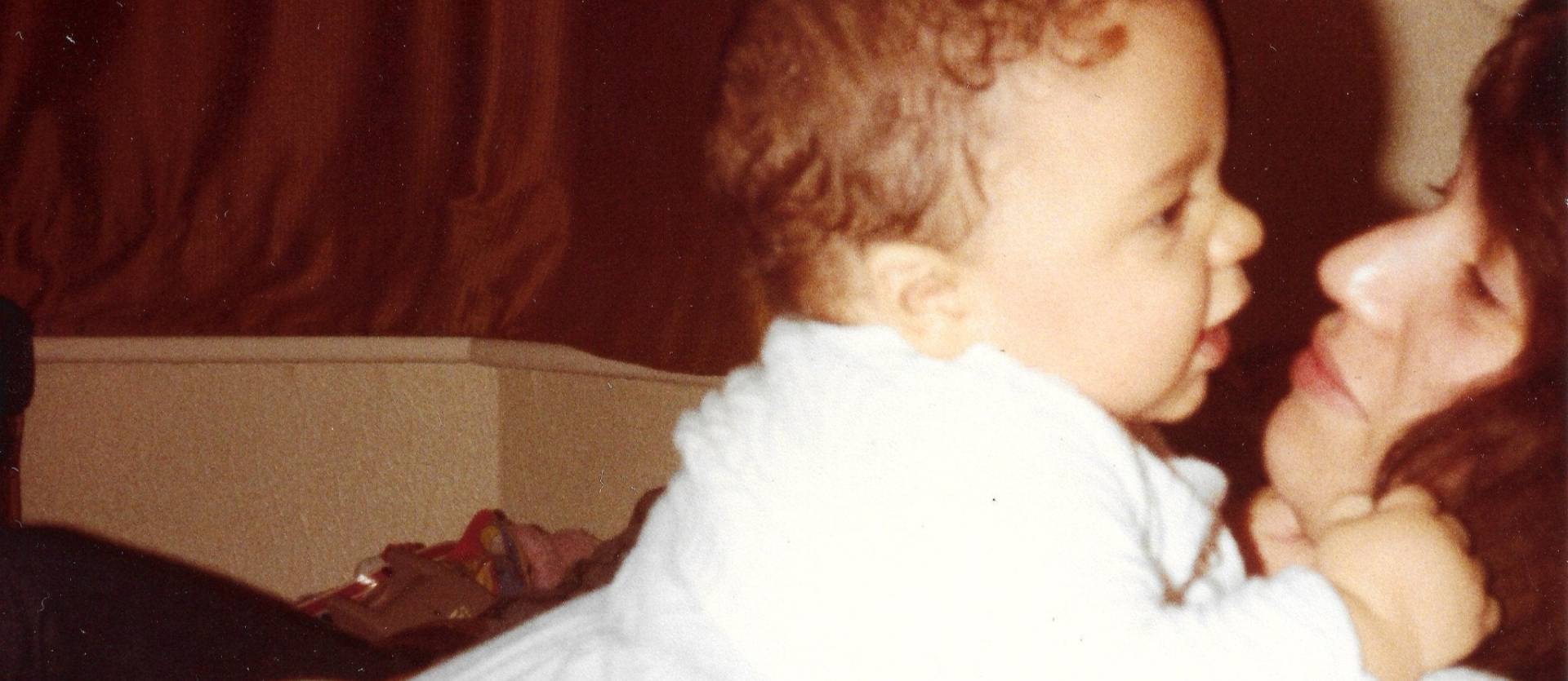 Baby in a white outfit being held by an adult with a blurred background