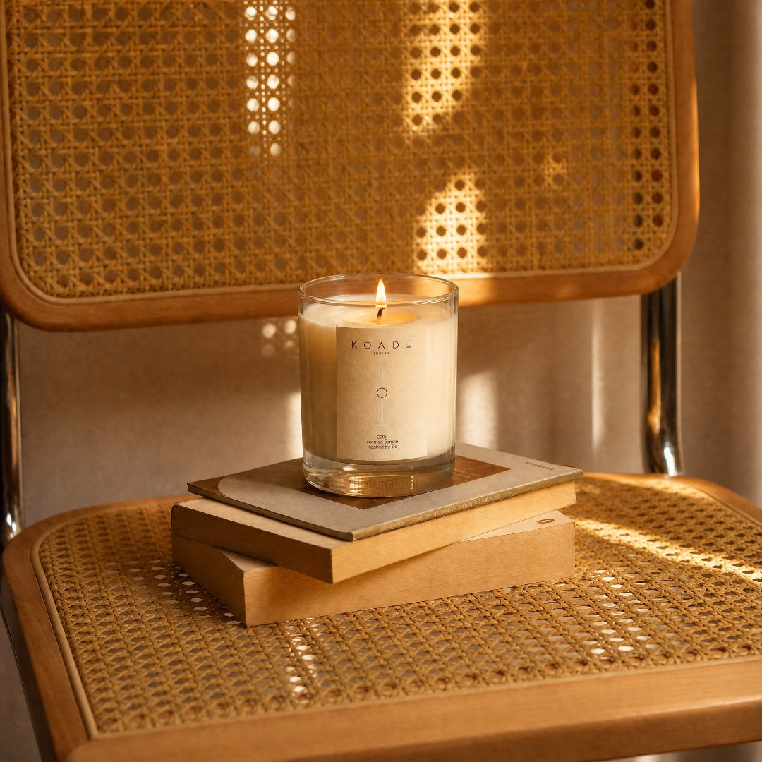 Candle labeled 'KOADE' on a coaster with woven chair back in the background