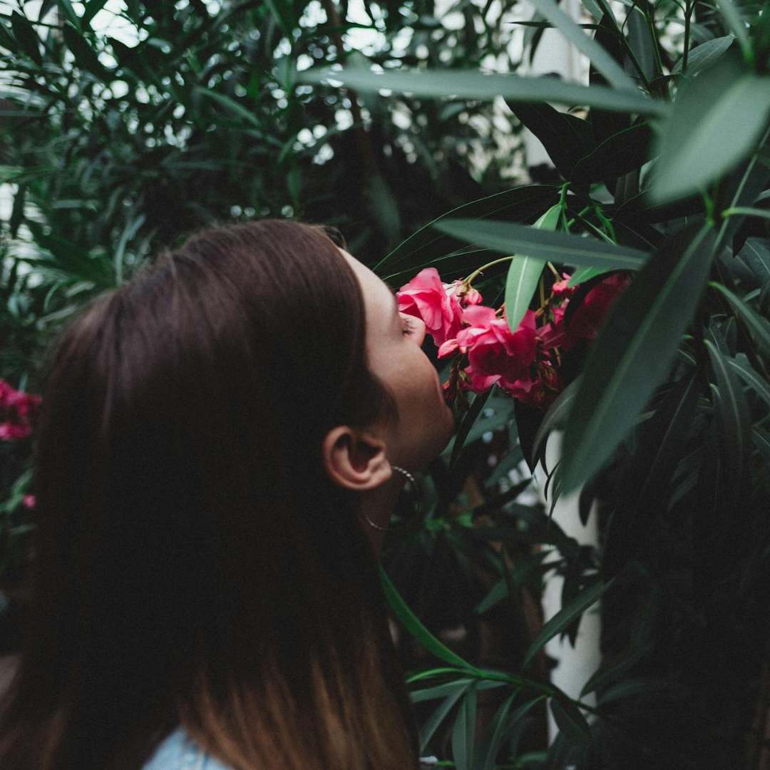 Woman smelling pink flowers amidst green foliage