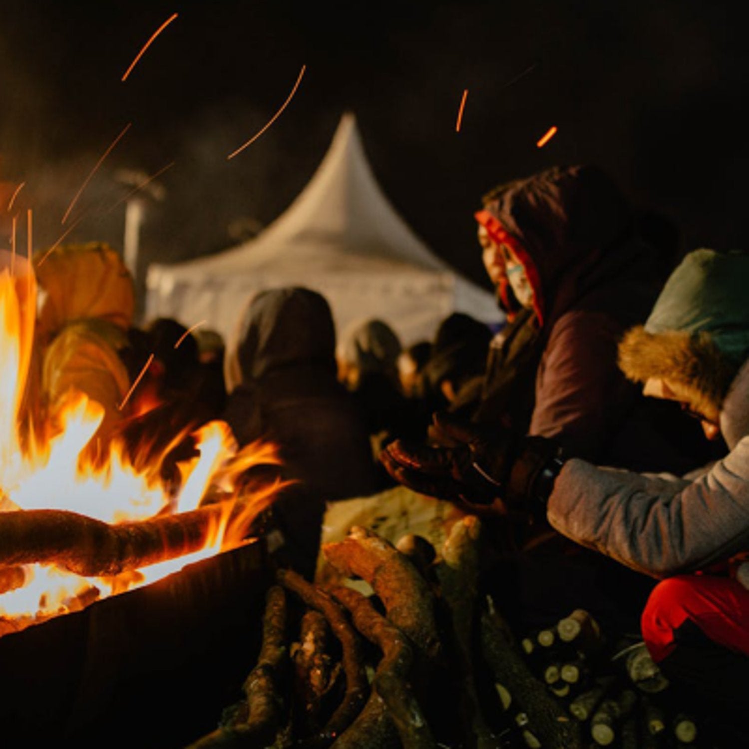 People around a bonfire at night with a tent in the background
