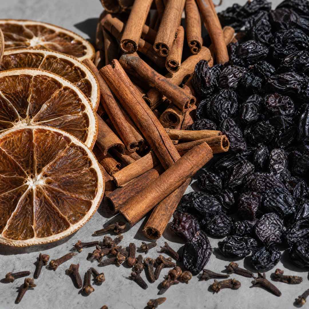 Spices including cinnamon sticks, dried orange slices, and raisins on a gray surface