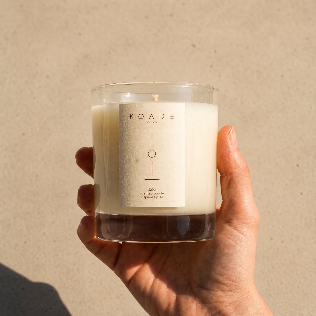 Hand holding a KOADE candle against a beige background