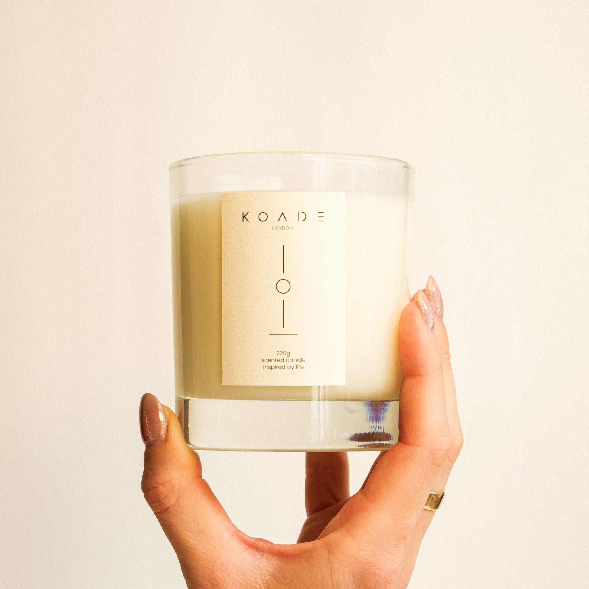 Hand holding a KOADE candle against a plain background