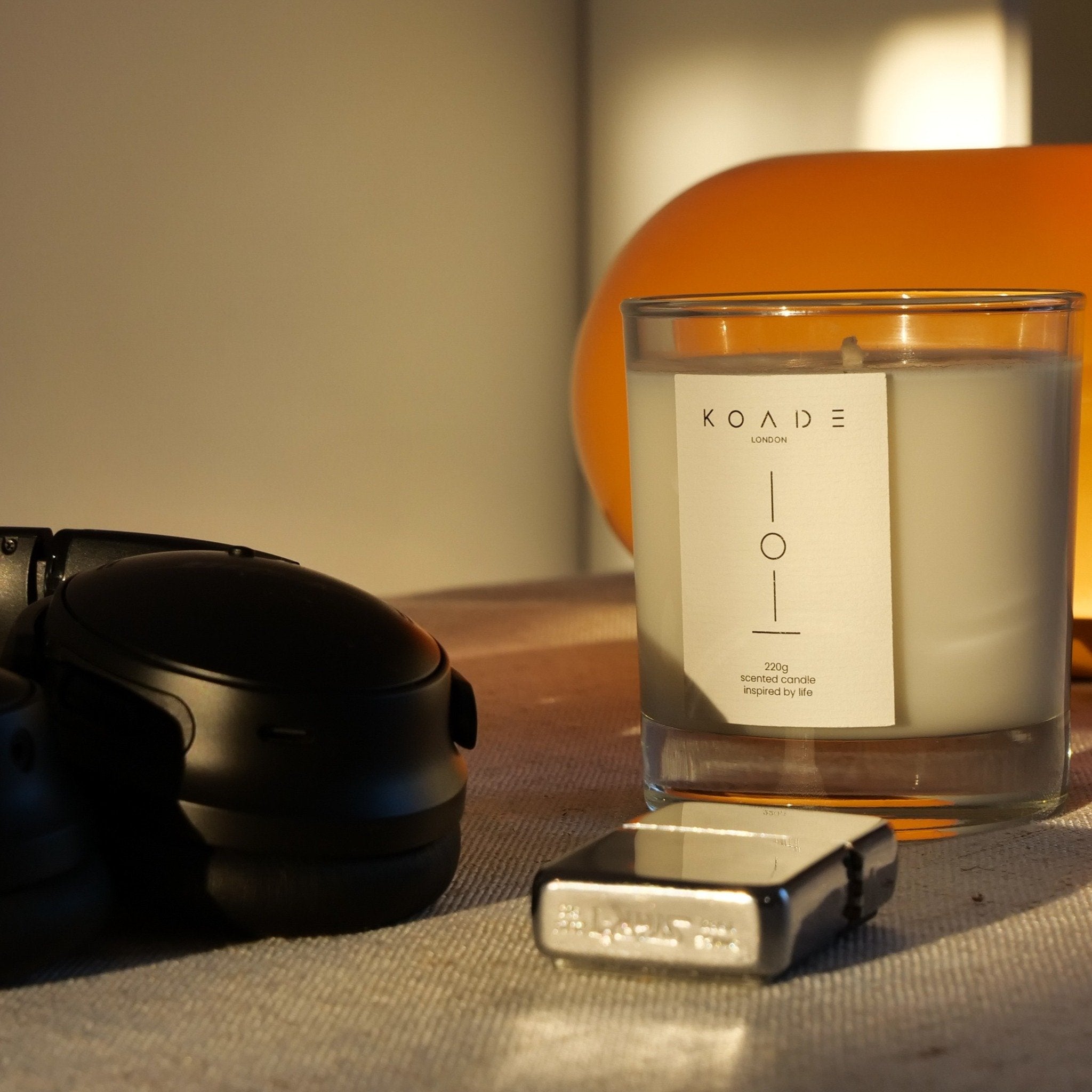 Candle with a label, lighter, and black container on a textured surface.