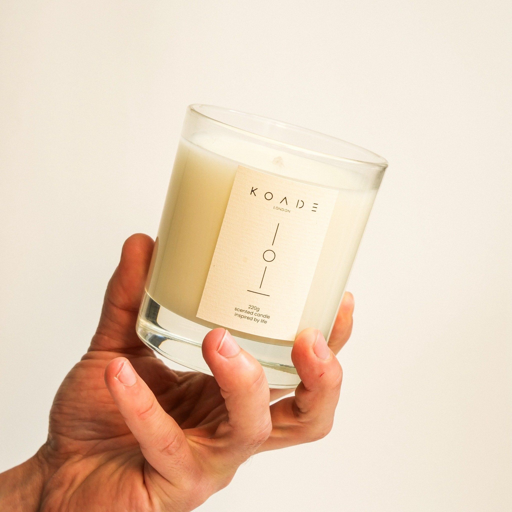 Hand holding a KOADE candle against a plain background