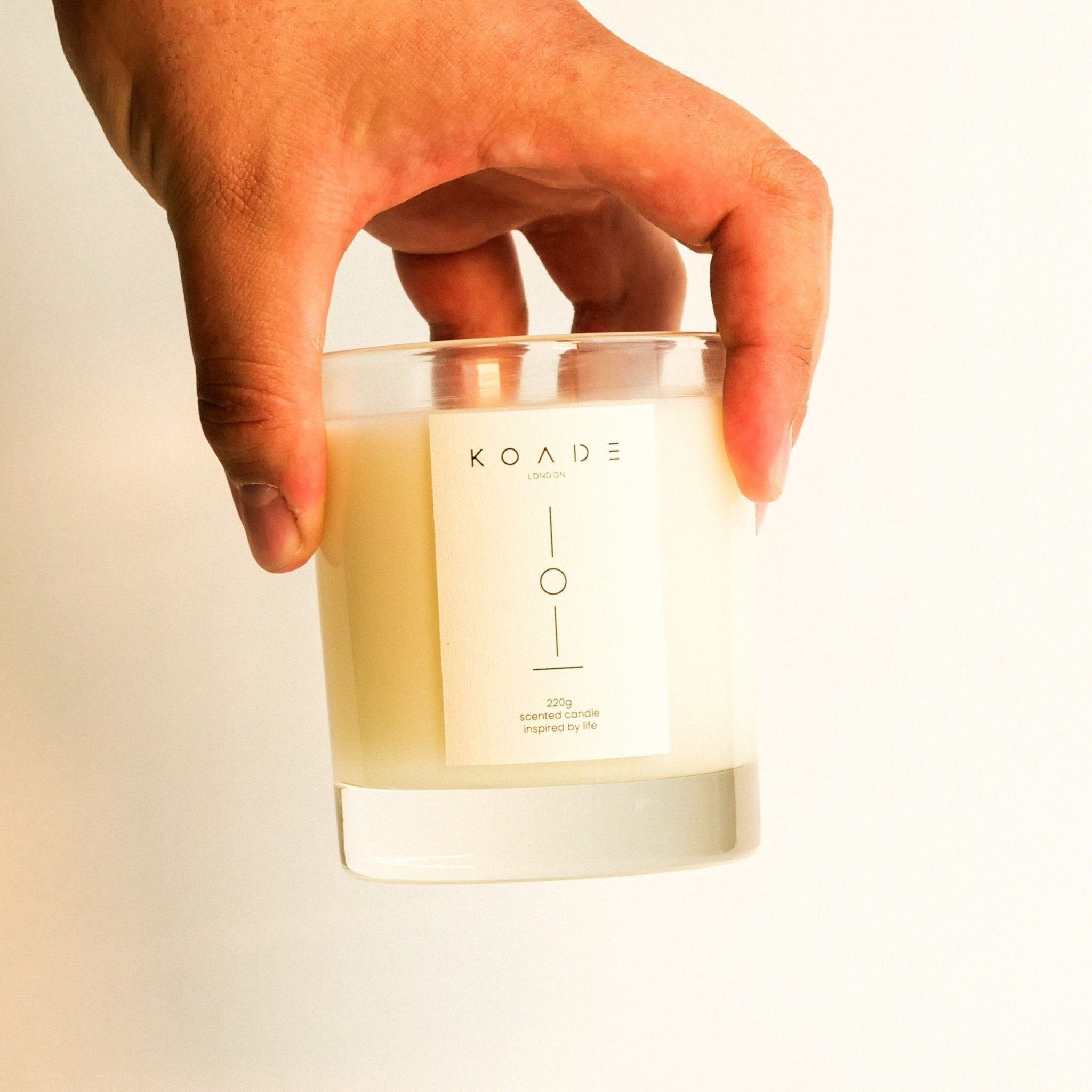 Hand holding a KOADE candle against a plain background