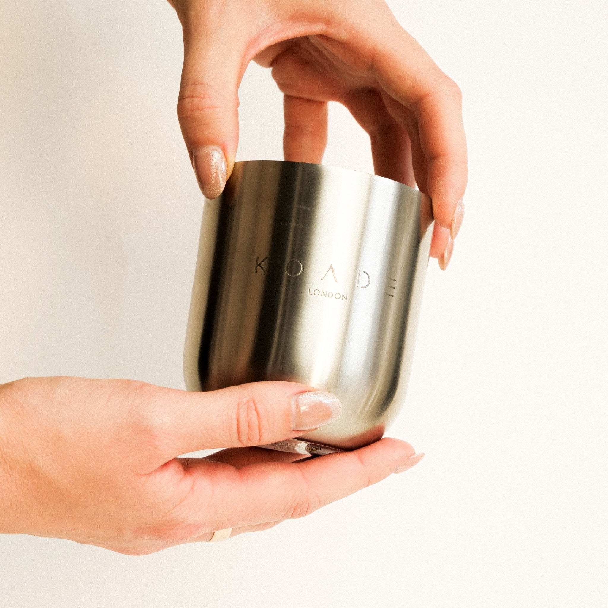 Silver cylindrical container held by a hand with a plain background