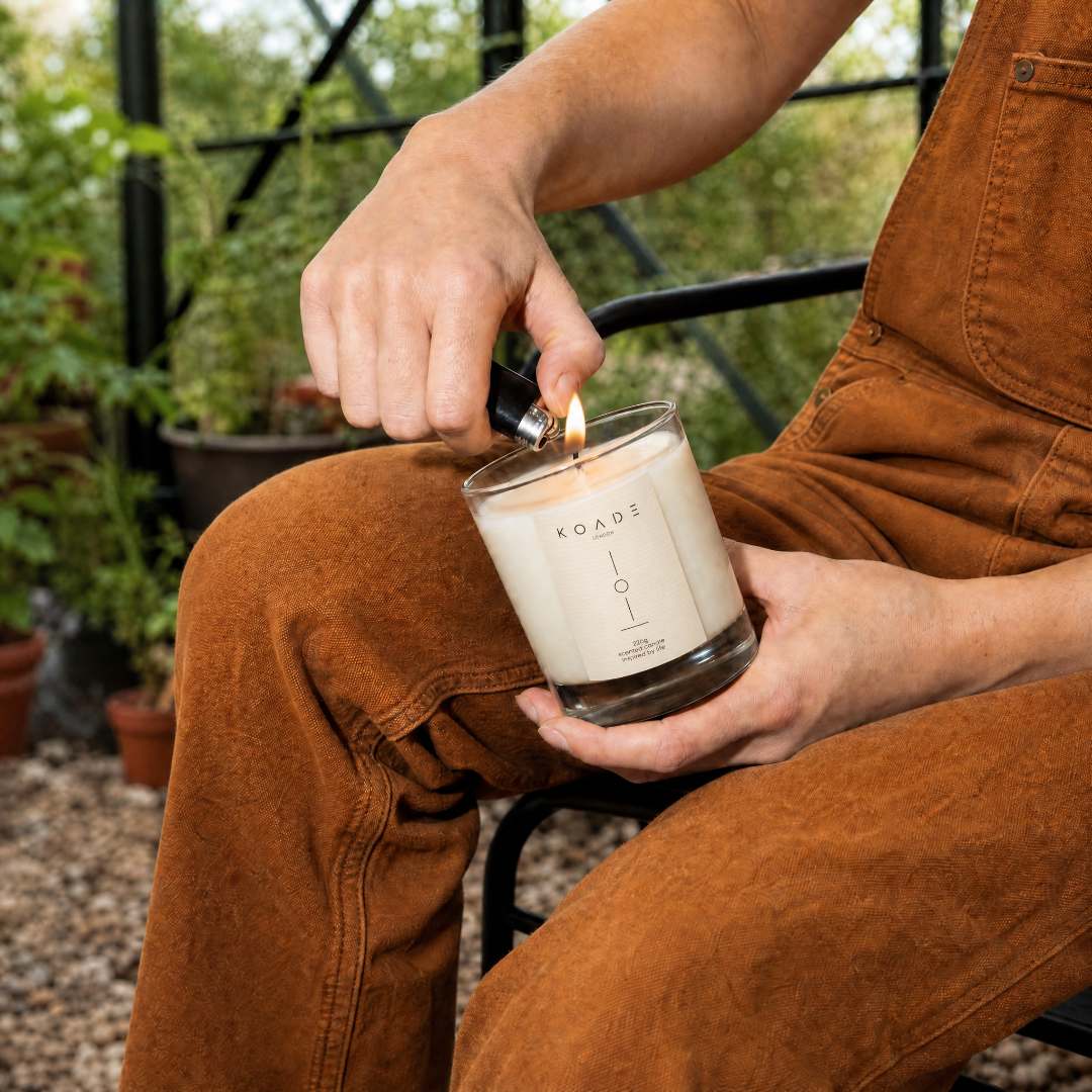 Person lighting a candle labeled 'KOADE' outdoors.