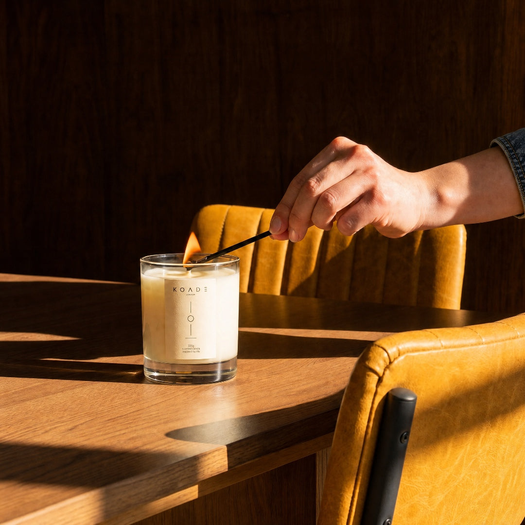 Candle on a wooden table with a hand holding a spoon, surrounded by warm lighting.